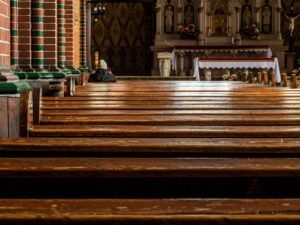 Burnout pastoral: pessoa orando sozinha em igreja com bancos de madeira e altar iluminado, símbolo de descanso espiritual